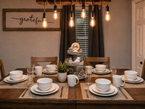 Et spisebord dækket med hvide, mønstrede skåle, tallerkener og kopper, med et skilt med ordet 'grateful' over bordet og et skilt med ordet 'Gather' på en etagestativ.