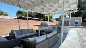 Un patio al aire libre con mobiliario de mimbre, una parrilla y un área techada.