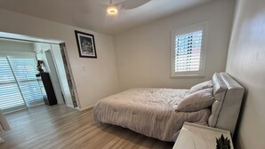 Un dormitorio con cama, ventana, ventilador de techo y planta en maceta.