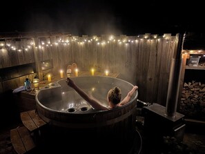 Un bain à remous dans un chalet en bois rustique, agrémenté de guirlandes lumineuses et de bougies.