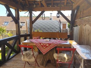A wooden deck with a table and chairs, a large tree trunk, and a view of buildings in the background.