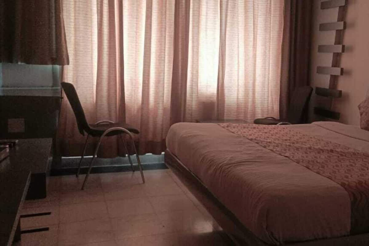Un dormitorio con cama, una silla, un escritorio y una ventana con cortinas.