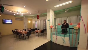 A hotel reception area with a modern design, featuring a curved reception desk, a television mounted on the wall, and a seating area with tables and chairs. - Grande Sita Hotel (Udaipur)