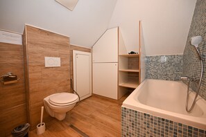 A modern bathroom with a wooden floor, a white toilet, a white bathtub, and a shower. - Kitz Residenz Twelve View of the River (Kaprun)