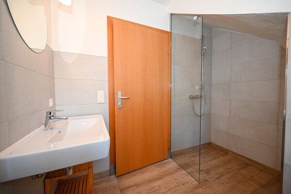 A bathroom with a white sink, wooden door, and a glass shower enclosure. - Kitz Residenz Twelve View of the River (Kaprun)