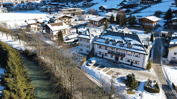 Un villaggio innevato con edifici tradizionali, un fiume e montagne sullo sfondo.