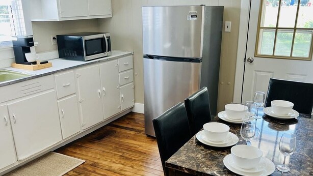 A modern kitchen with white cabinets, a stainless steel refrigerator, a microwave, and a dining table set with white plates and glasses.