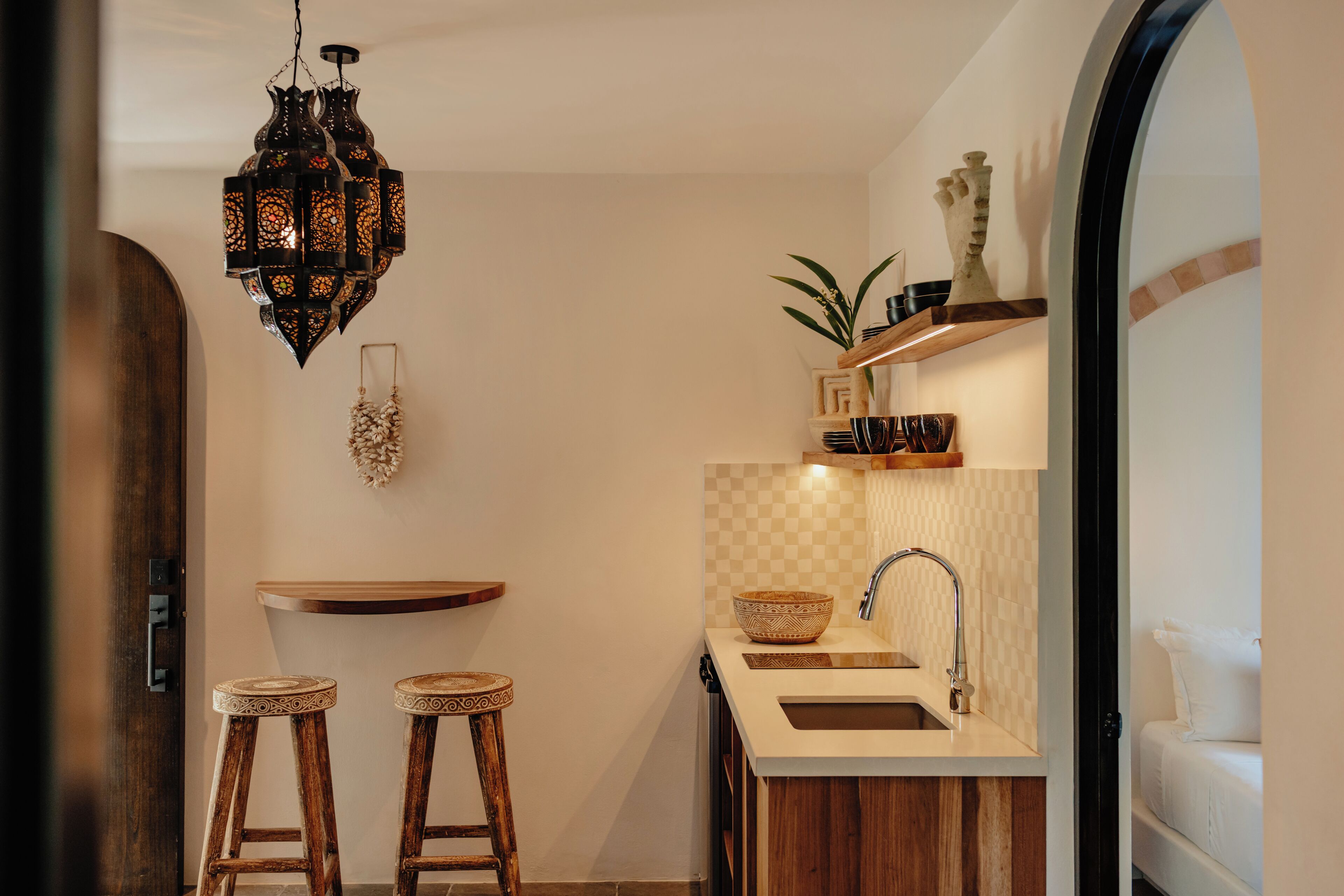 A compact kitchen with a wooden countertop, two stools, a hanging lantern, and a sink.