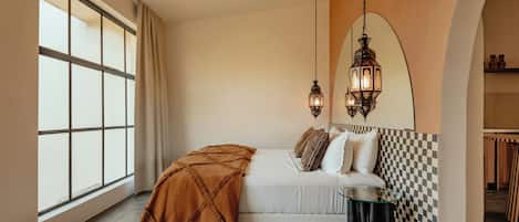 Une chambre avec une grande fenêtre, un mur à carreaux, un lit avec des oreillers, un luminaire suspendu et une petite table.