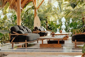 A tropical outdoor seating area with wooden furniture, a surfboard, and lush greenery. - Domo Nosara Boutique Hotel (Nosara)