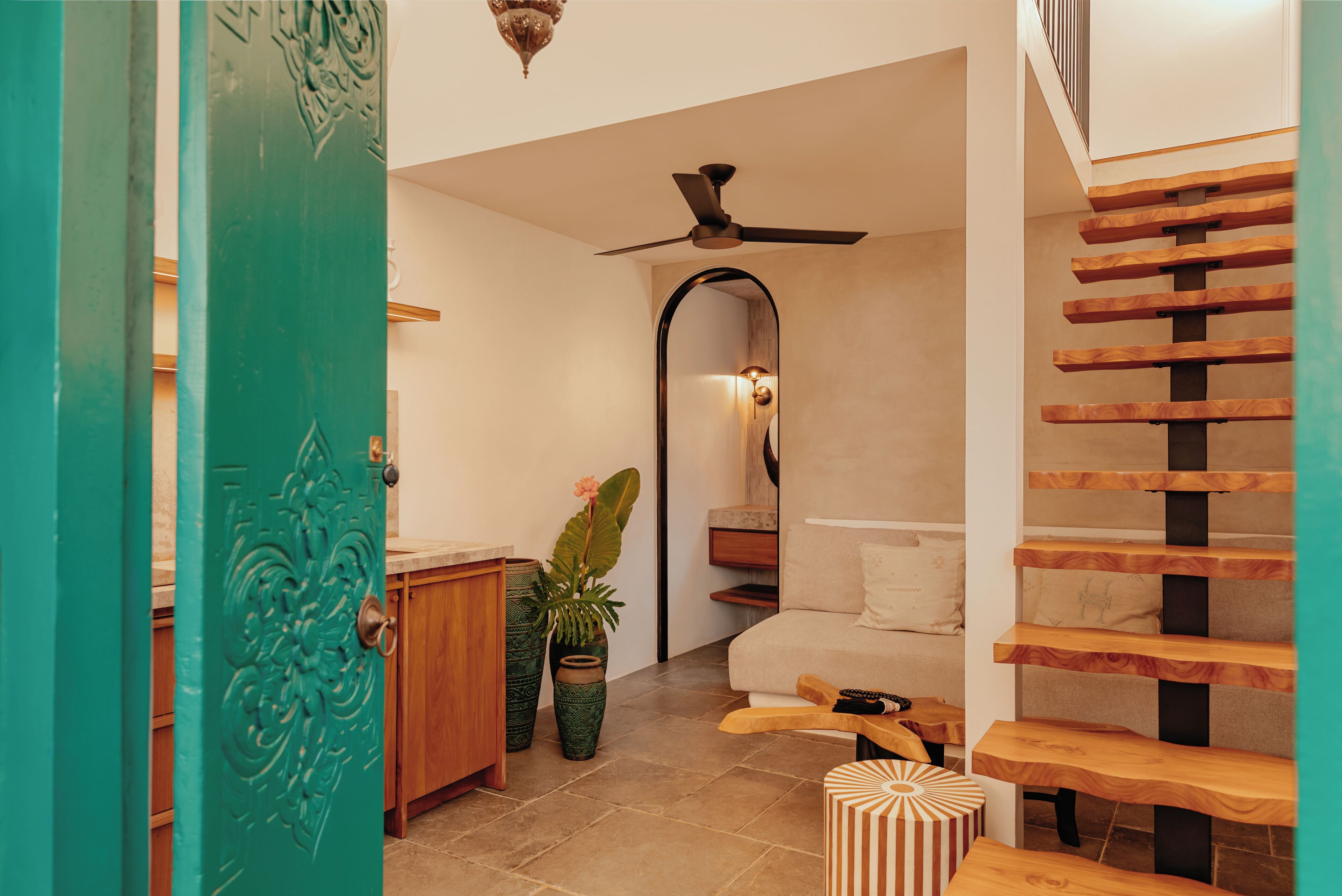 Un corridoio con una porta color acquamarina, una ventola a soffitto, una scala e una panca di legno.