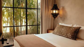 A bedroom with a large window, a bed with a brown blanket, a patterned pillow, and a hanging lantern.