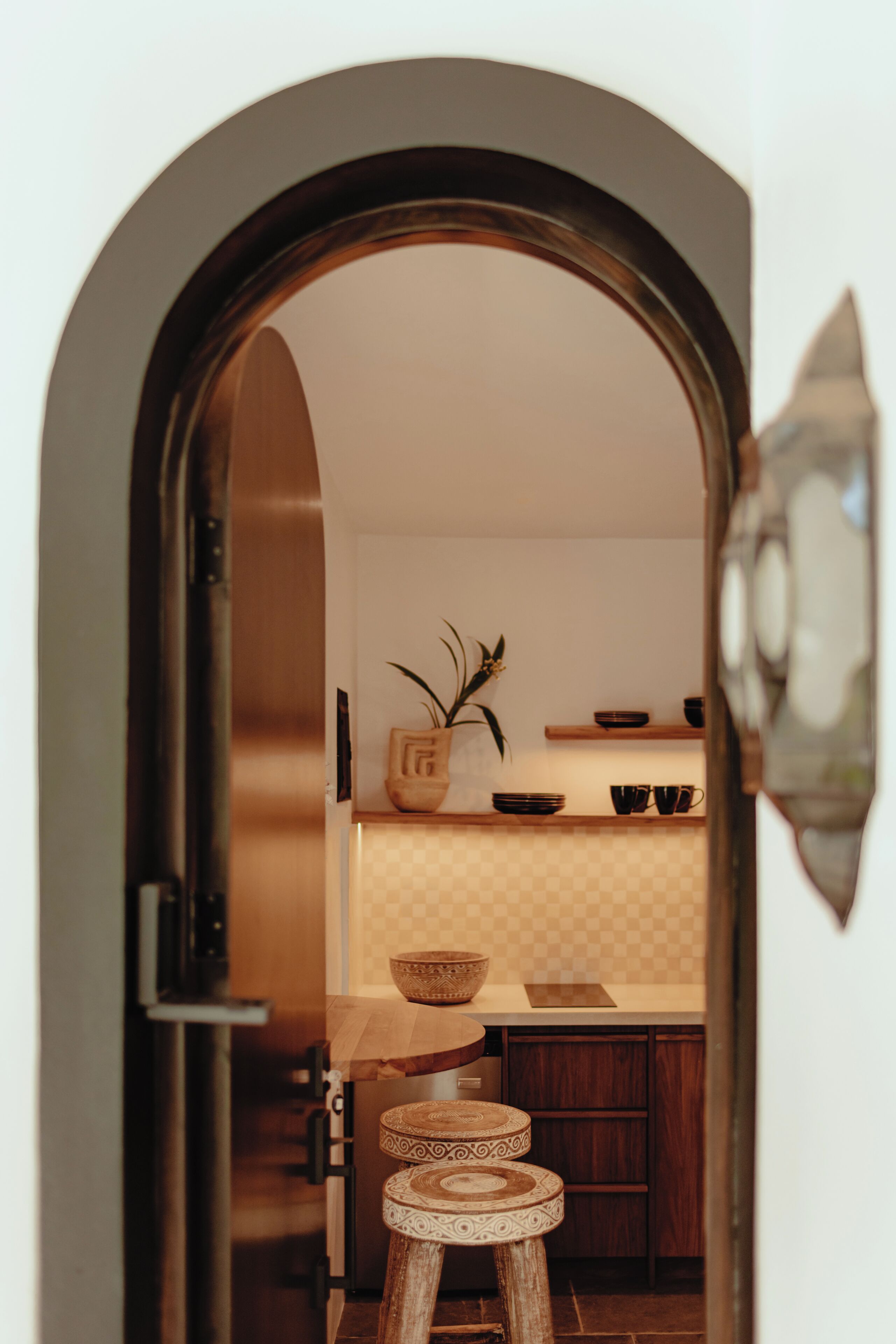 Un arco de entrada que da a una cocina con un taburete de madera, un cuenco y una planta.