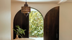 Ein Zimmer mit einem runden Holztisch, einer hängenden Laterne und einem großen, bogenförmigen Durchgang zu einem Garten.