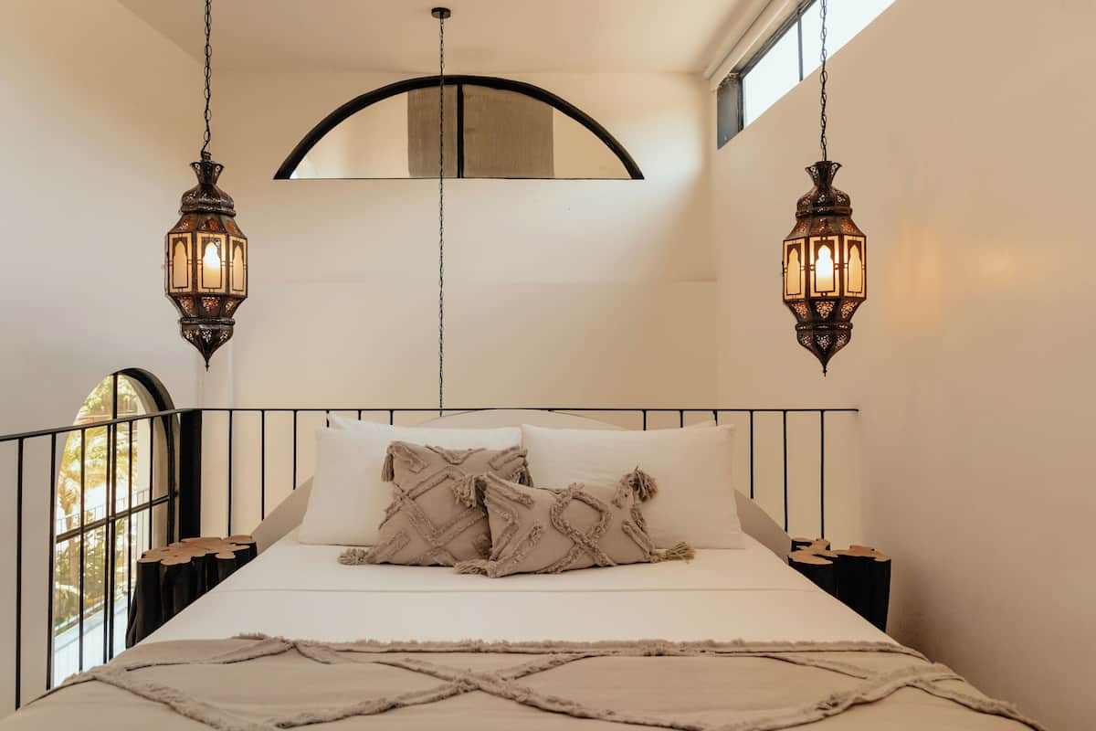 Una cama con cabecera, dos faroles colgantes, una ventana y una vista parcial de una puerta.