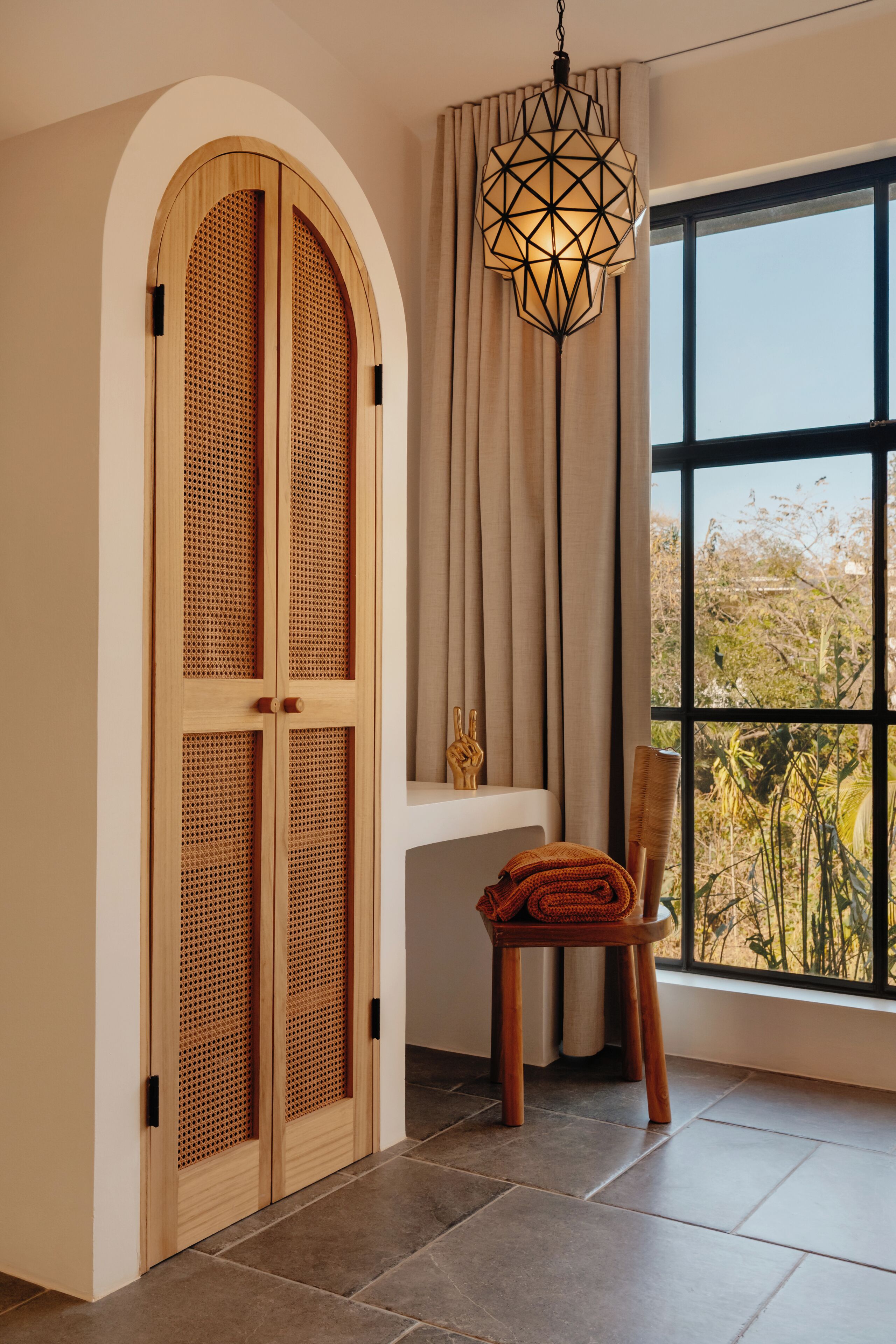 A room with a large window, a wooden door with a lattice design, a hanging light fixture, and a chair with a towel.