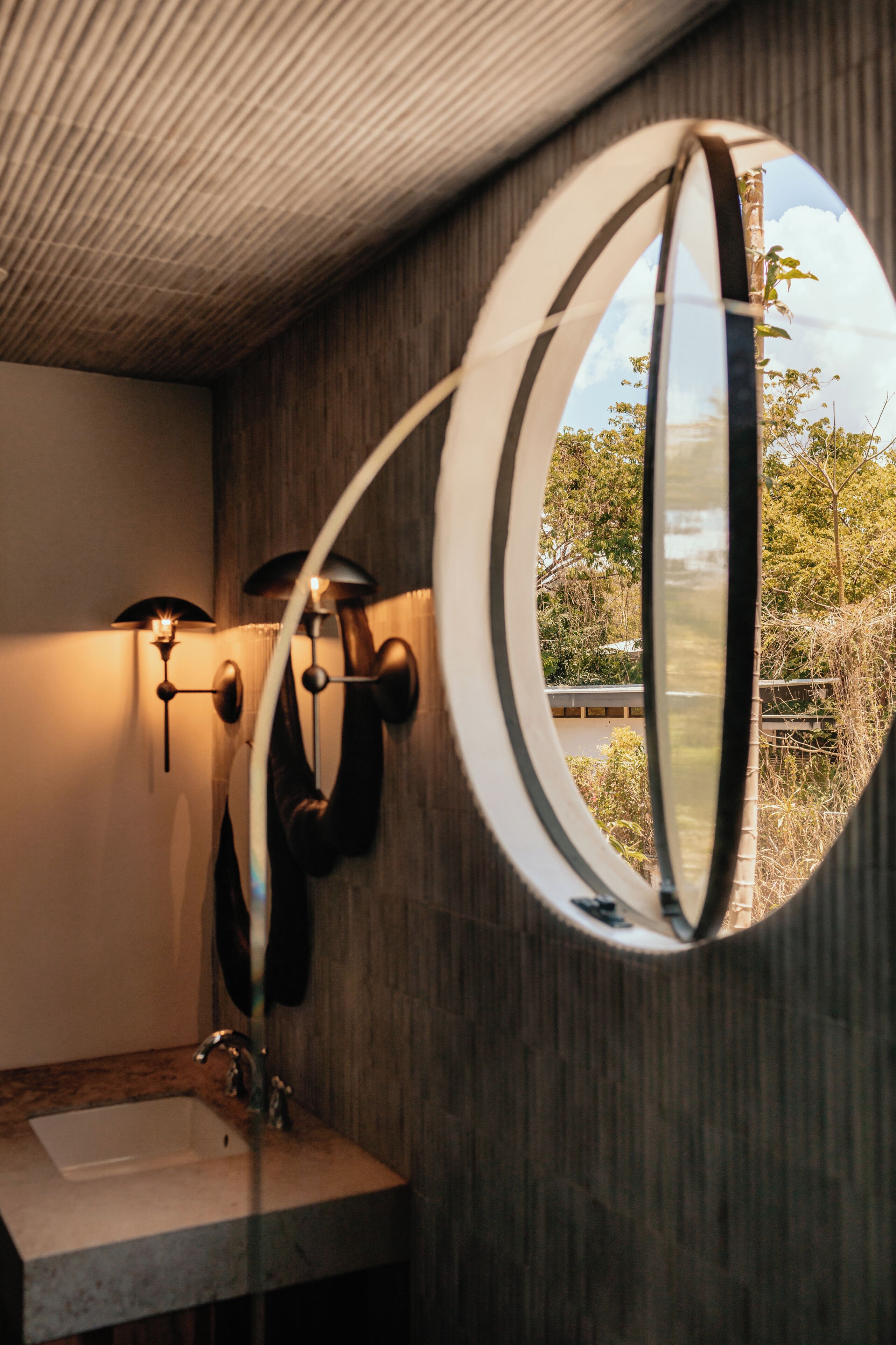 Une salle de bain avec un miroir rond, un lavabo et des luminaires fixés au mur.