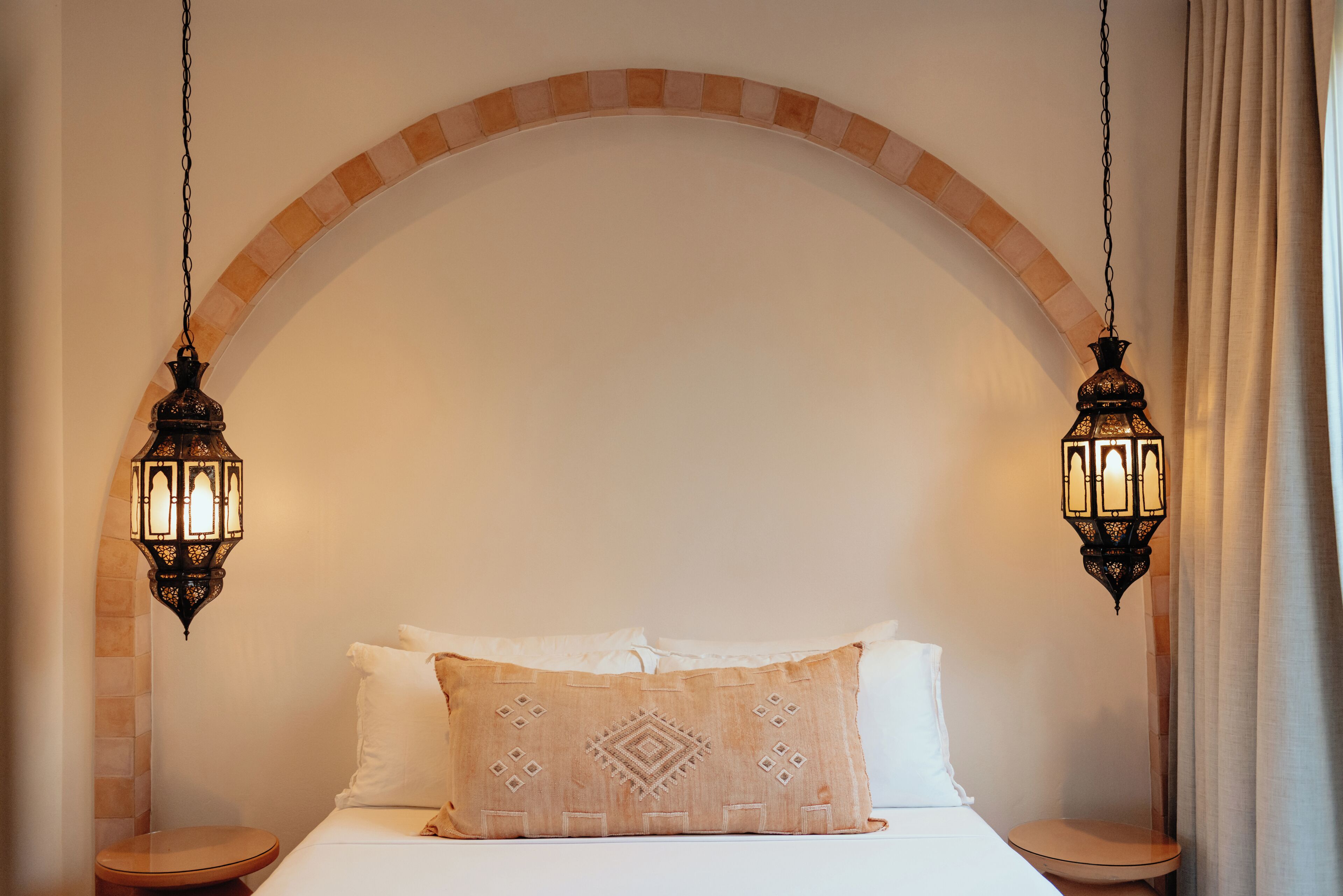 A bed with a patterned pillow, two hanging lanterns, and an arched ceiling.