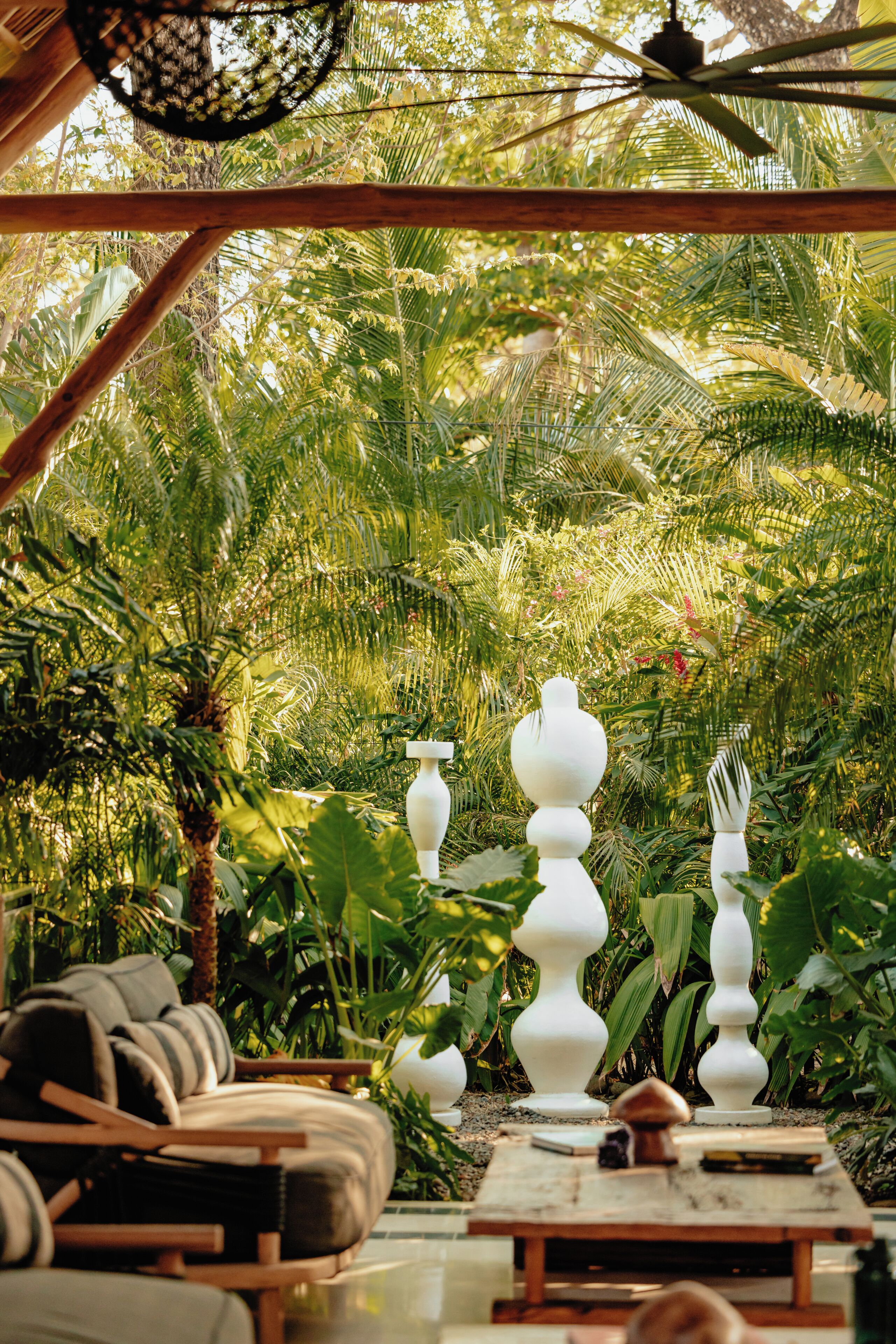 Un jardín tropical con una mesa de madera, jarrones blancos y un ventilador de techo.