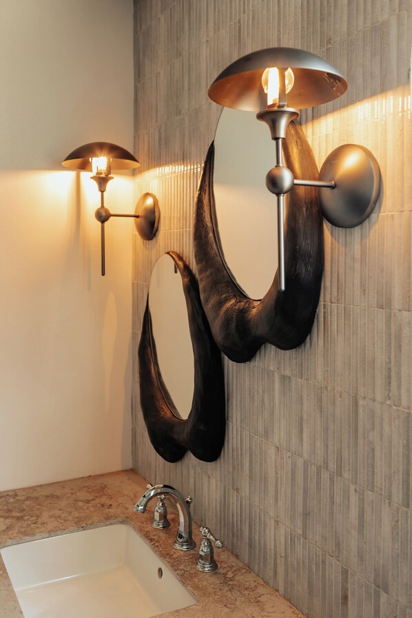 A bathroom with a modern design, featuring a large mirror, a sink, and two wall-mounted light fixtures.