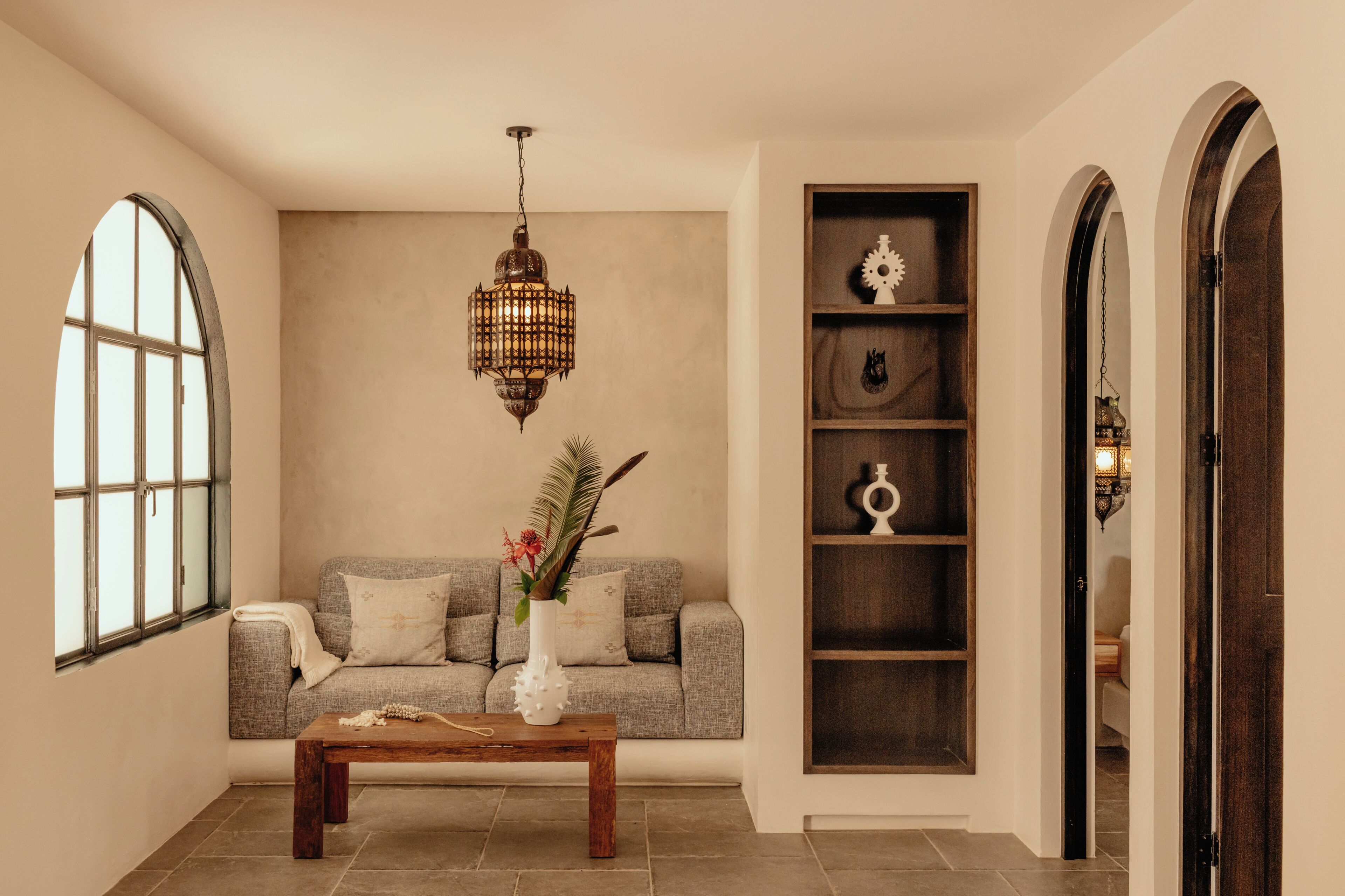 A room with a sofa, a wooden coffee table, a decorative vase, a hanging lantern, and a wooden shelving unit.