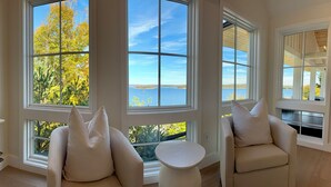 A room with large windows offering a view of trees and a body of water. There are two chairs and a small table.