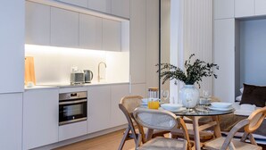 A modern kitchen with a dining area. It includes a kitchen island with a built-in oven and a coffee machine. There is a dining table with chairs and a vase with flowers.