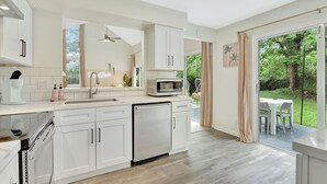 Uma cozinha moderna com armários brancos, lava-louças, micro-ondas e uma grande janela com vista para um jardim.