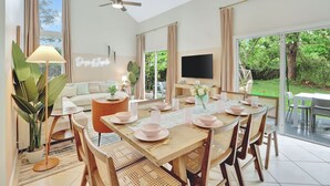 Uma sala de jantar moderna com uma mesa grande posta para seis pessoas, um ventilador de teto e uma televisão ao fundo.