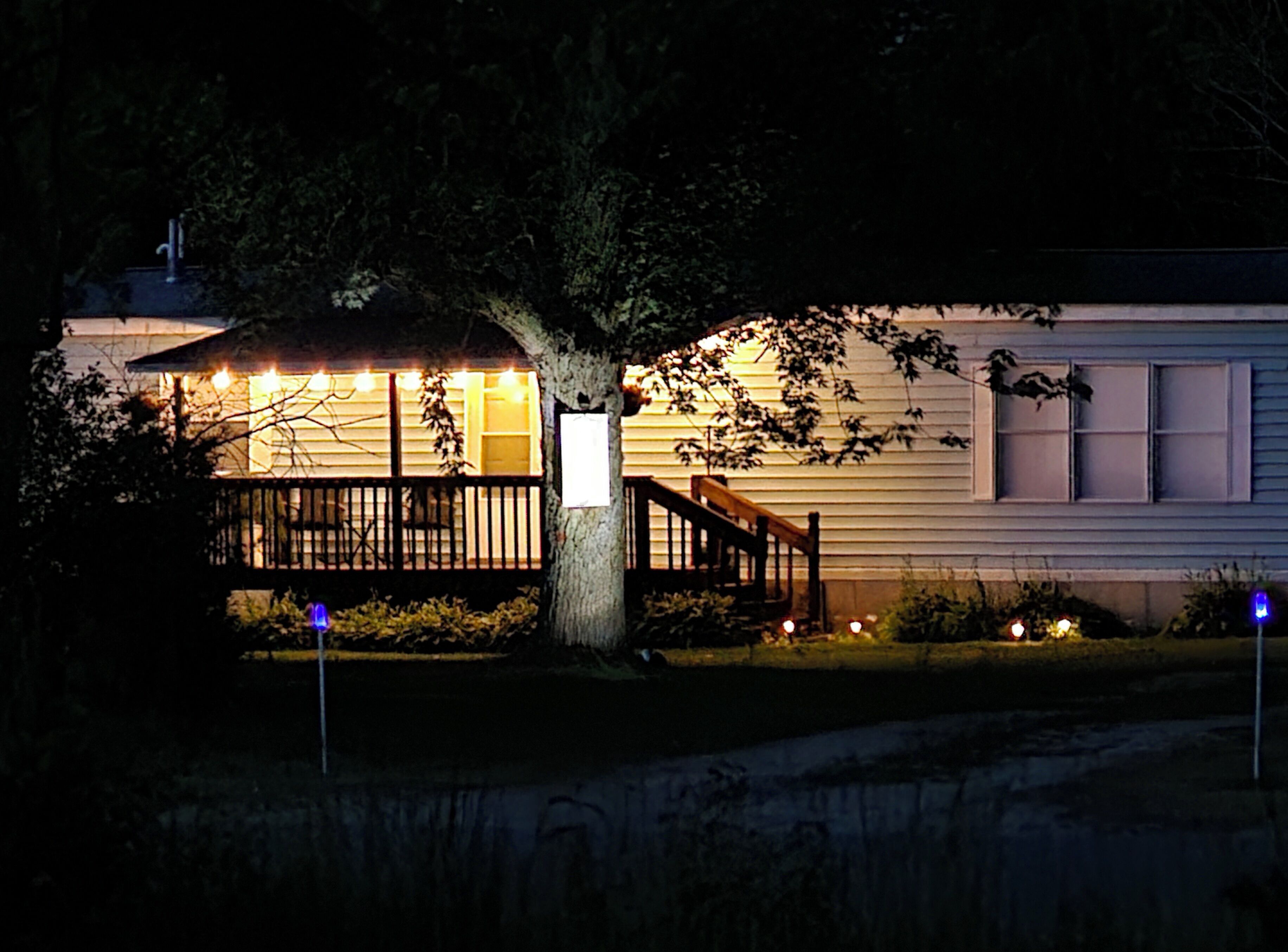 A house with a porch, a tree, and a well-lit exterior.