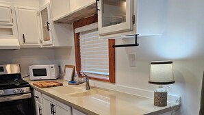A kitchen with white cabinets, a microwave, a stove, a sink, and a trash can. - Thoughtfully Renovated 2BR Retreat|10 Miles to South Haven & Lake Michigan (Bangor)