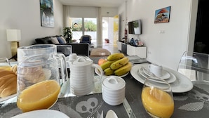 A dining area with a table set for breakfast, including fruits, a pitcher, and a glass of orange juice.