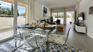 A modern living room with a glass dining table, clear chairs, and a sofa.