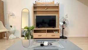 A modern living room with a flat-screen TV on a wooden TV stand, a painting above the TV, a small fan, and a coffee table with a geometric rug. - Transparent hosting devoid of excessive fees and stress-free check-in procedures (Lapu-Lapu City)