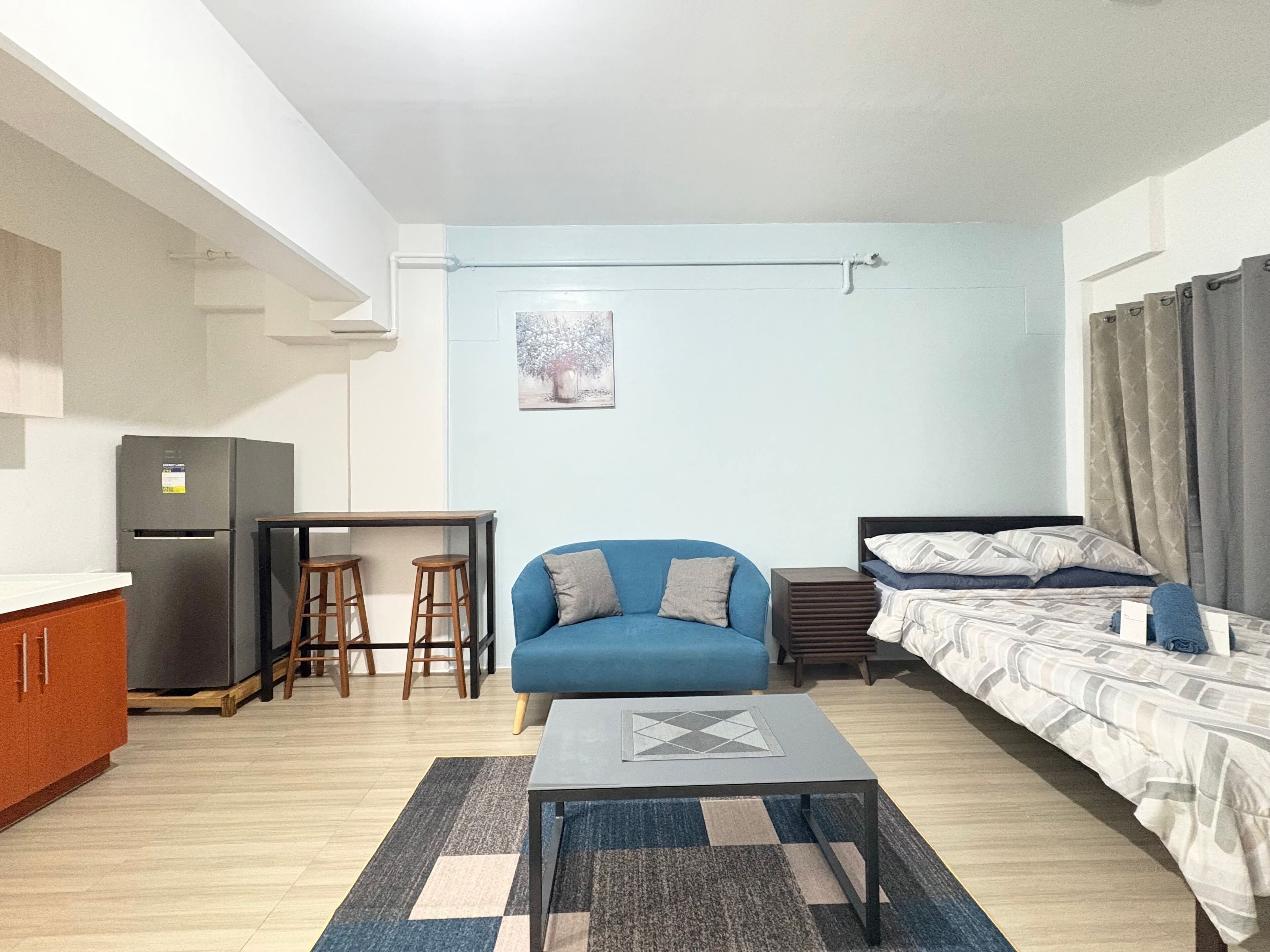 A compact living space with a kitchenette, a blue sofa, a bed, and a small table.