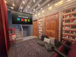 Une pièce chaleureuse avec un écran pour regarder Netflix, un tapis à motifs, un canapé et une bibliothèque agrémentée d’objets décoratifs.