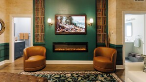 Een woonkamer met een open haard, twee leren fauteuils, een groene accentmuur en een ingelijst schilderij boven de open haard.
