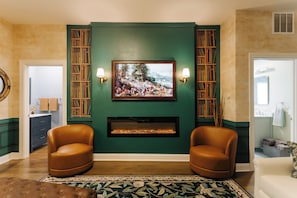 Un salon avec une cheminée, deux fauteuils en cuir, un mur d’accent vert et un tableau encadré au-dessus de la cheminée.