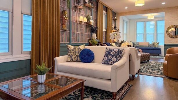 Een goed verlichte woonkamer met een witte bank, een glazen salontafel en een boekenkast vol boeken en decoratieve objecten.