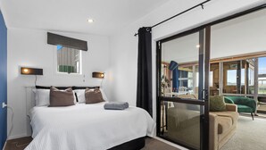 A modern hotel room with a large bed, a sliding glass door to a balcony, and a view of the outdoors.