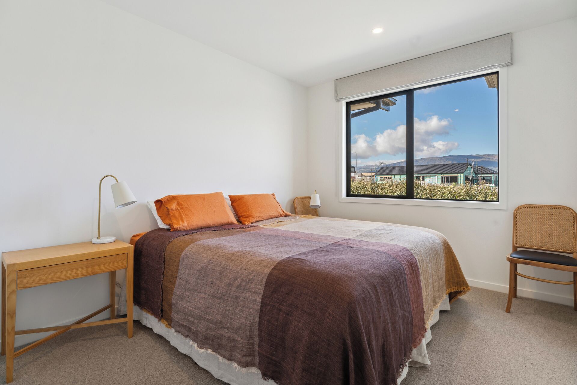 A bedroom with a large bed, a nightstand, a chair, and a window with a view of buildings.