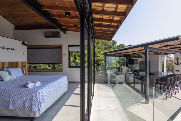 Un dormitorio moderno con cama, un ventanal grande y un balcón con barandilla de cristal.