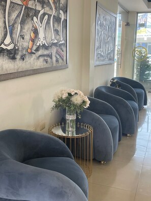Un interior moderno con una hilera de sofás azul oscuro, una mesa de centro de cristal con un arreglo floral y obras de arte abstracto en las paredes.