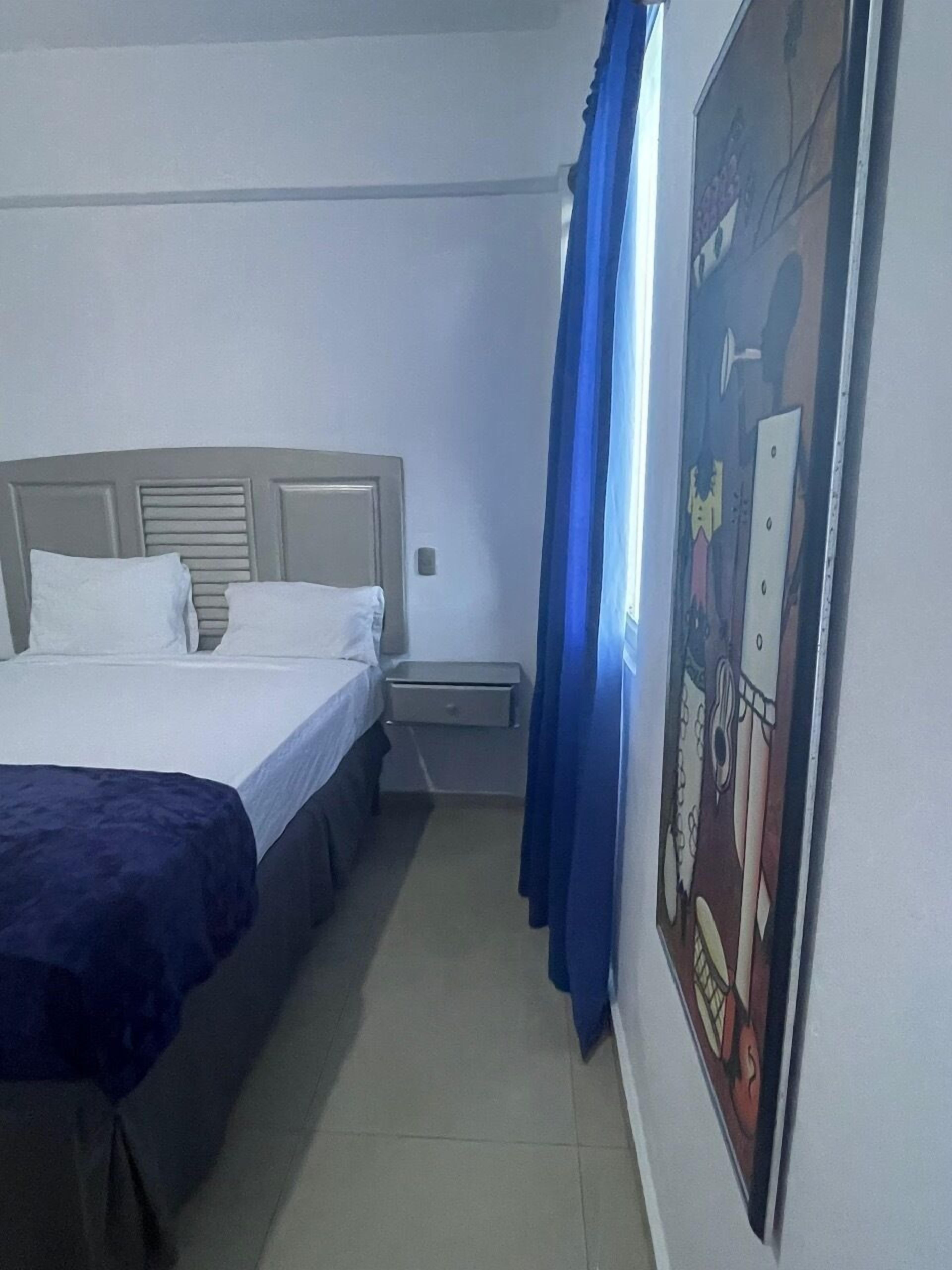 A hotel room with a bed, a nightstand, a wall-mounted heater, and a poster on the wall.