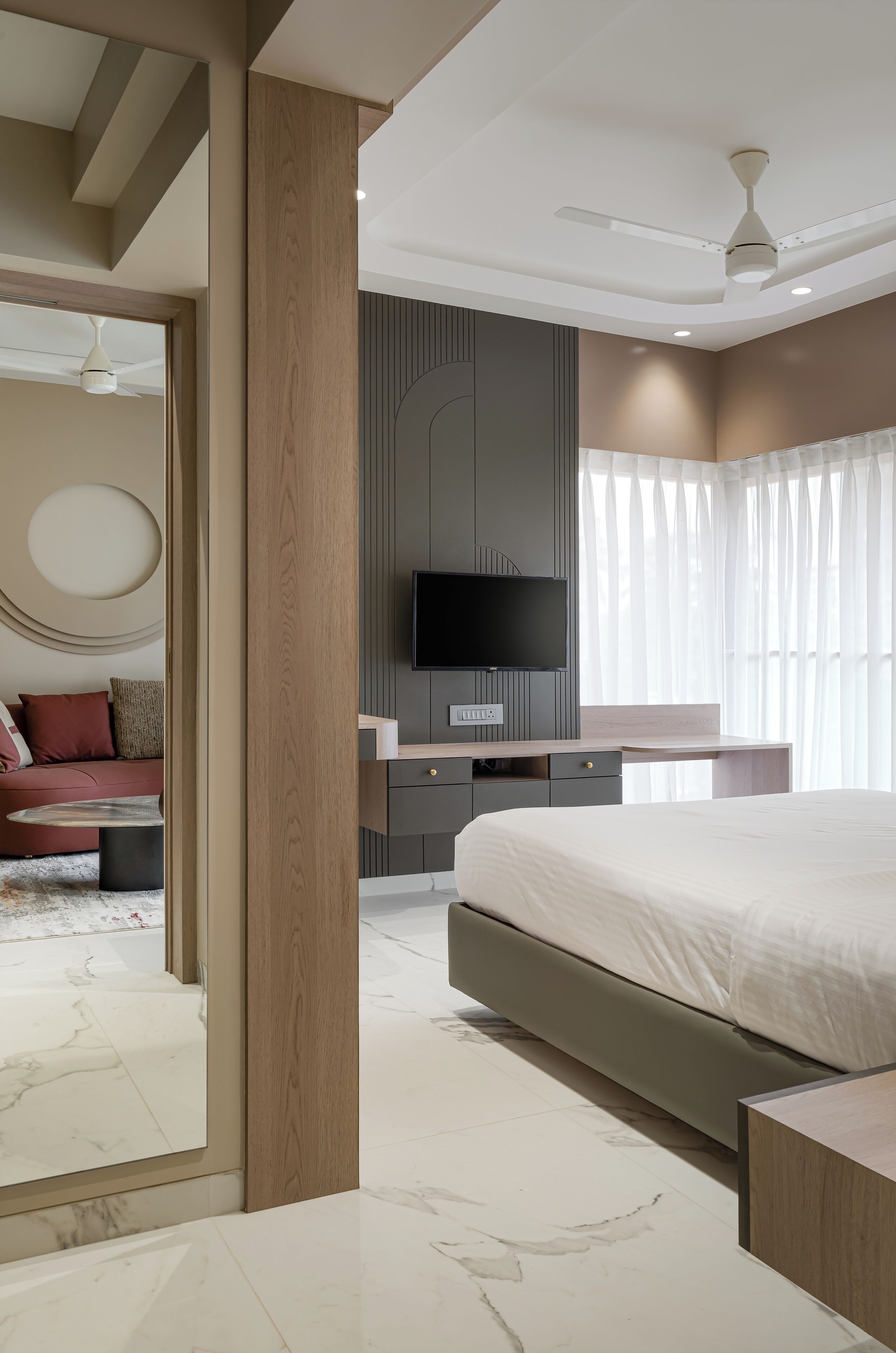 Un dormitorio moderno con una cama grande, un televisor instalado en un mueble oscuro y un ventilador de techo.