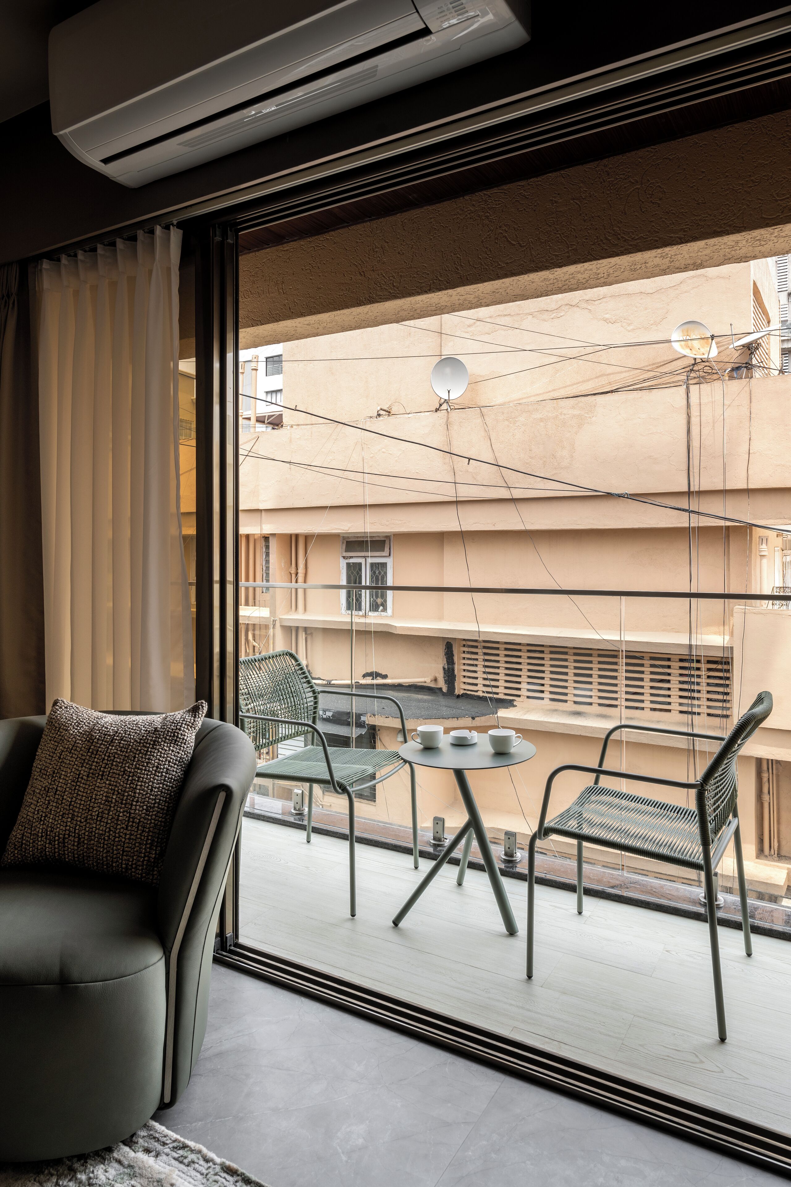 Un balcón con sofá y sillas, una mesa con tazas y vistas a edificios.