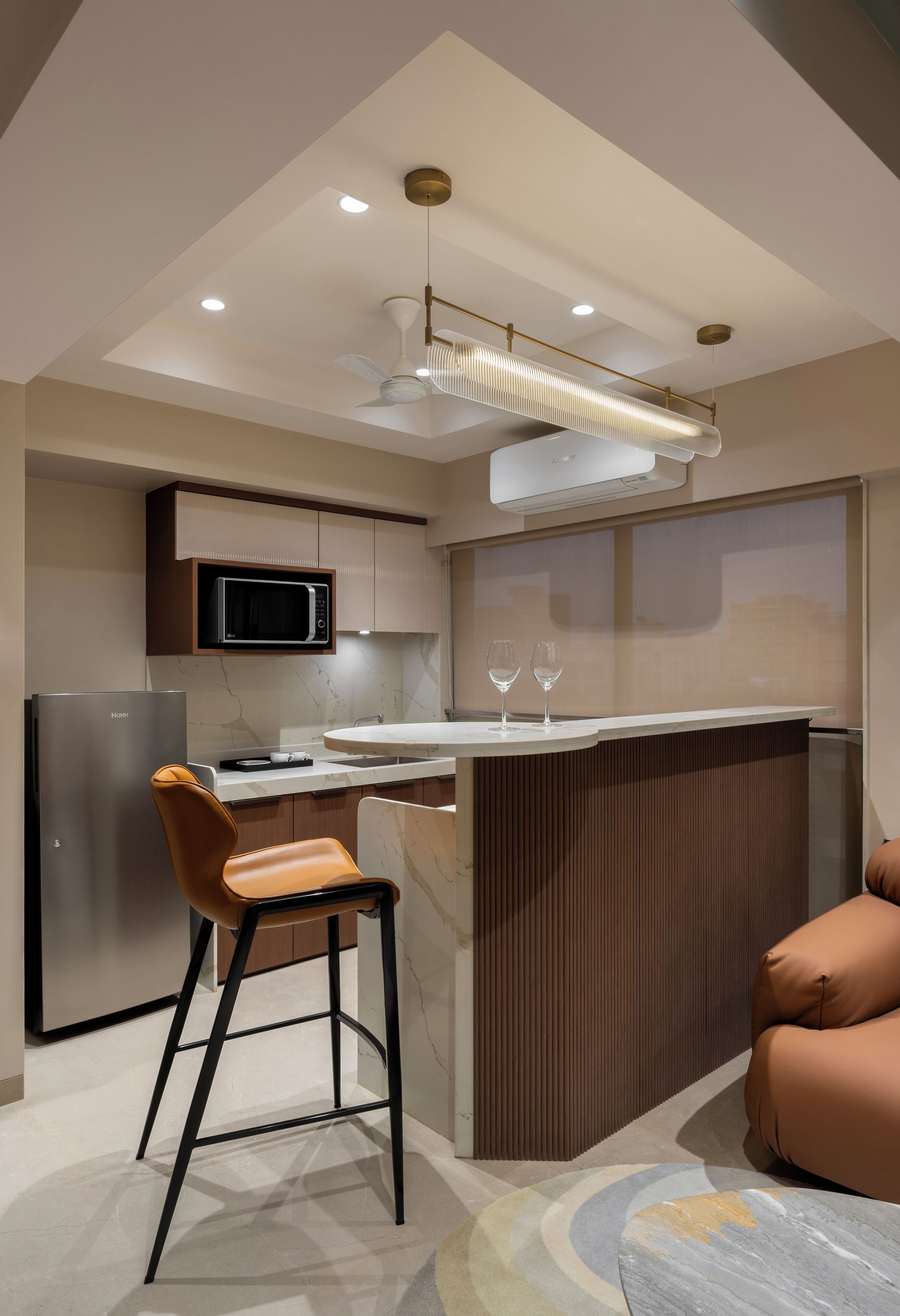 A modern kitchen with a central island, bar stools, a microwave, and a refrigerator.