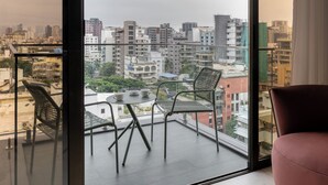 Un balcon avec vue sur la ville, une table avec des chaises et une chaise rouge.