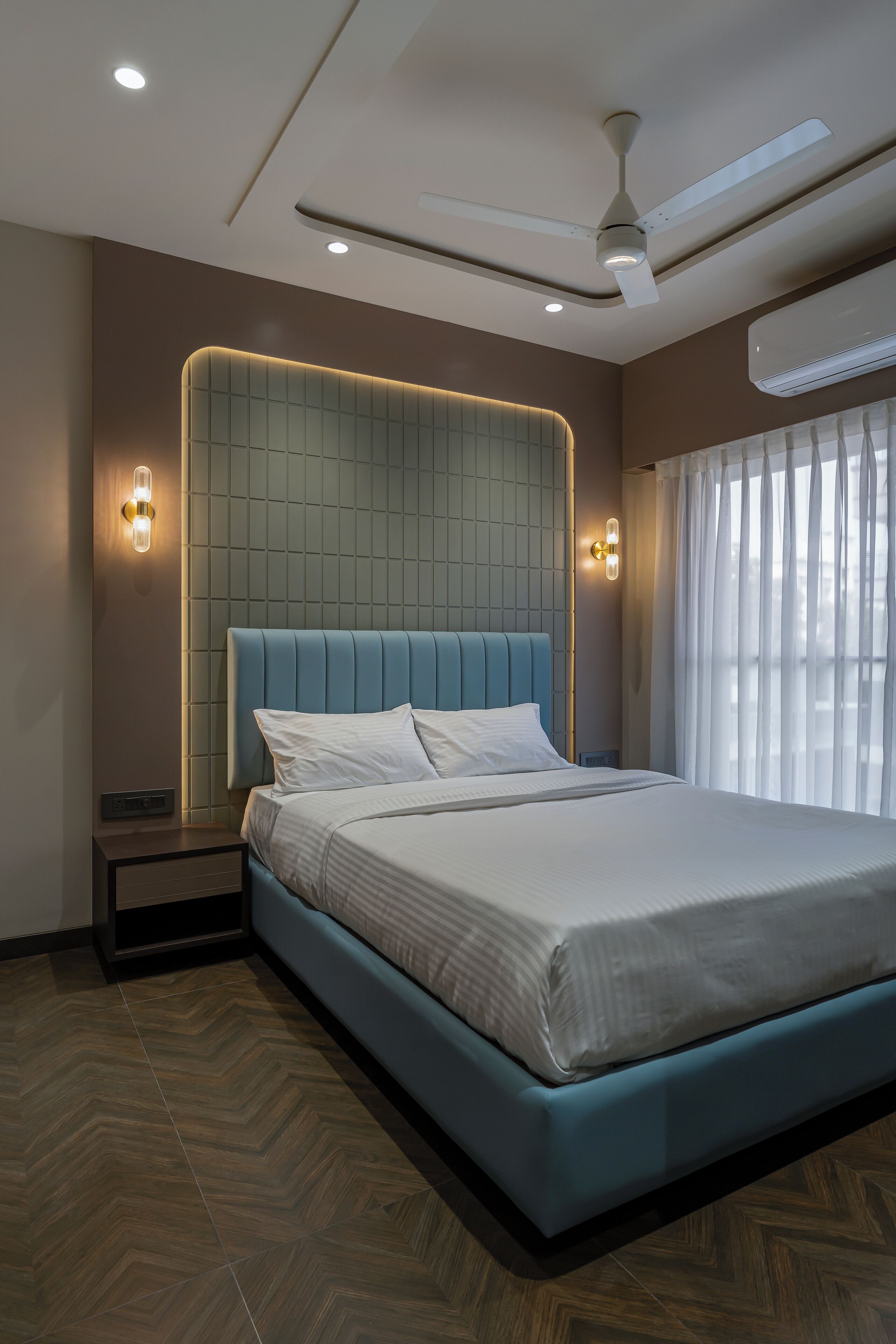Una habitación de hotel moderna con una cama grande, ventilador de techo, iluminación empotrada y aire acondicionado.