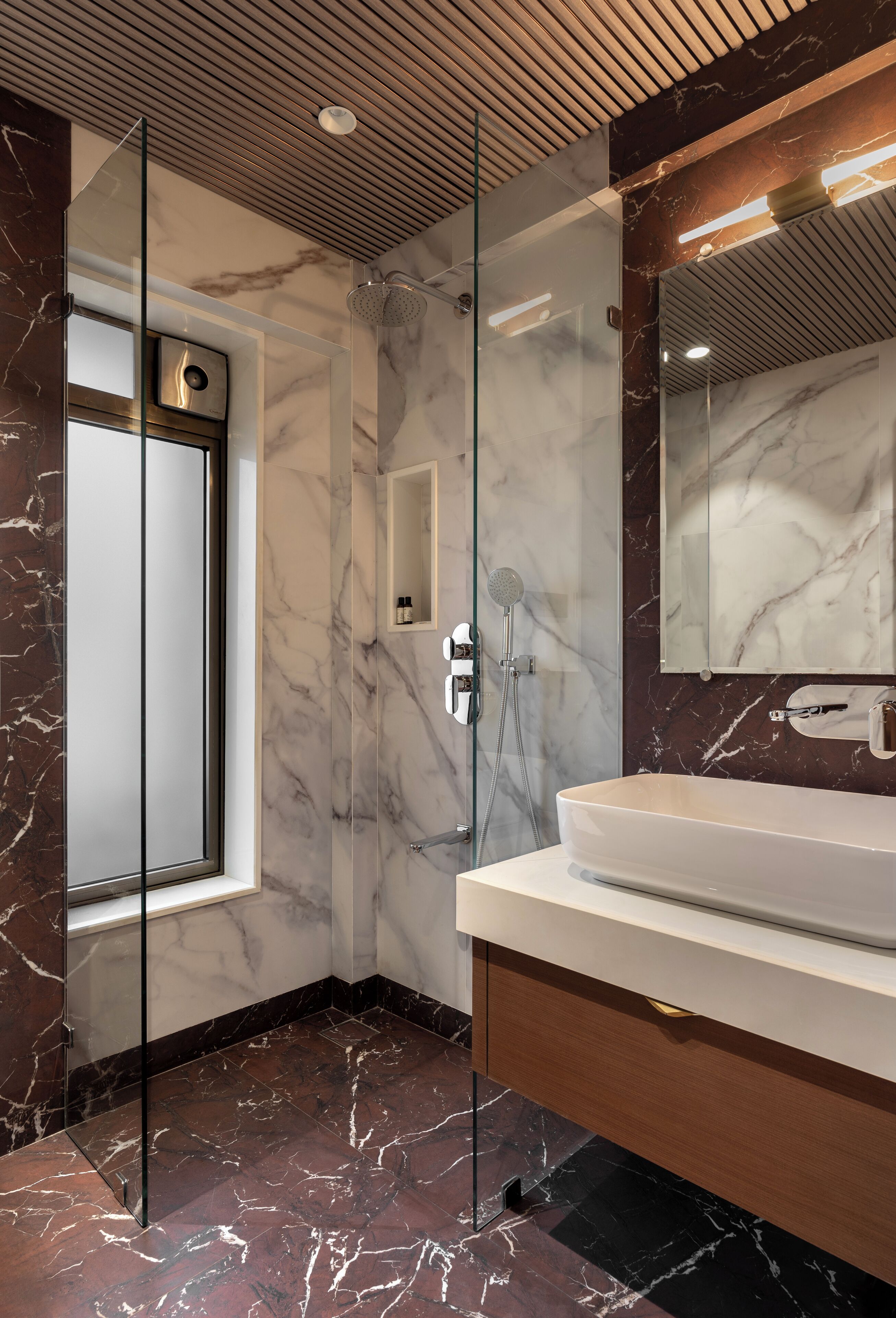 Un baño moderno con ducha envuelta en vidrio, suelo de mármol y un espejo grande sobre el lavamanos.